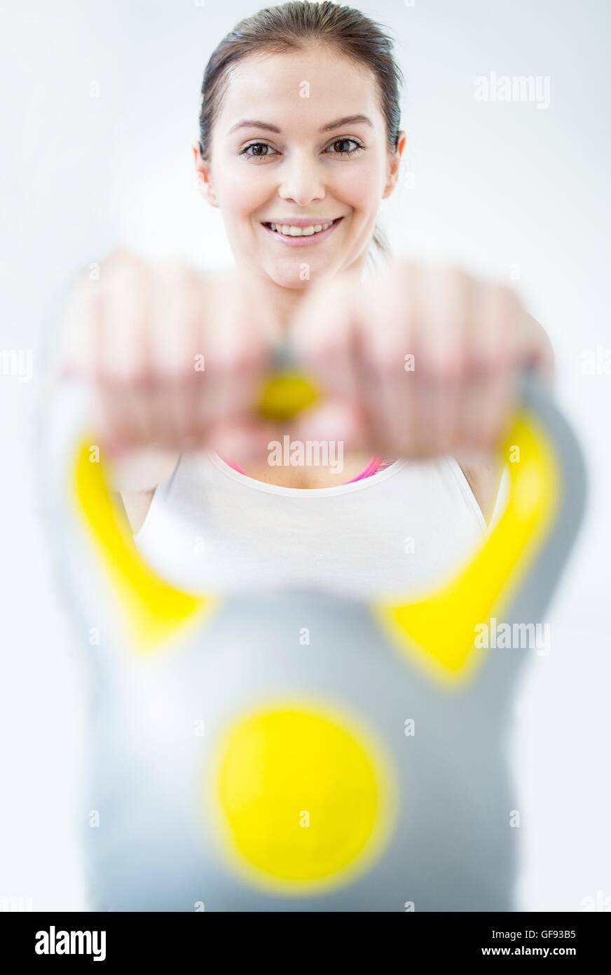 EIGENTUM FREIGEGEBEN. -MODELL VERÖFFENTLICHT. Lächelnde junge Frau mit Kettlebell im Fitness-Studio, Porträt. Stockfoto
