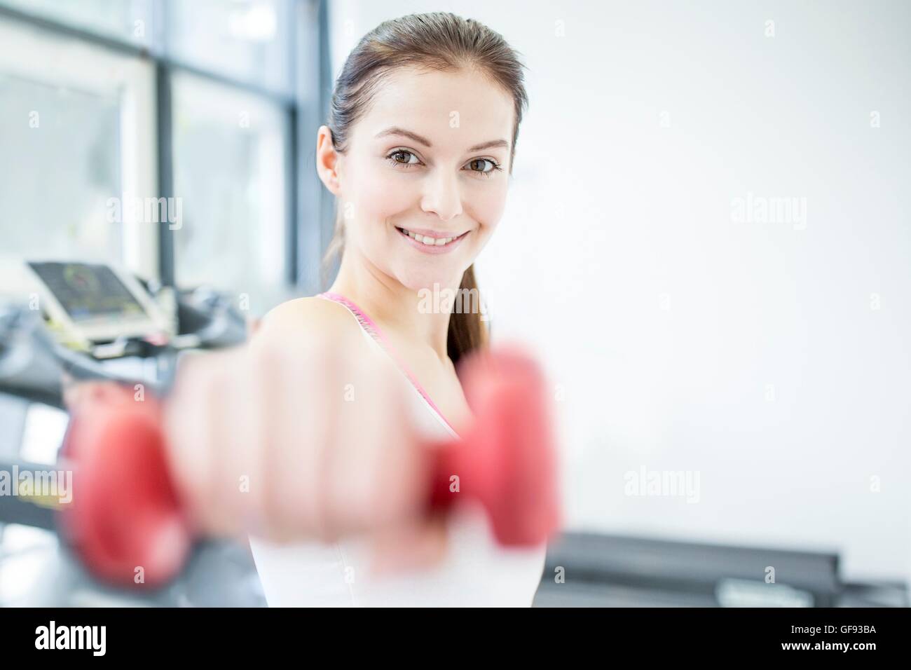 EIGENTUM FREIGEGEBEN. -MODELL VERÖFFENTLICHT. Lächelnde junge Frau mit Hantel im Fitness-Studio, Porträt. Stockfoto