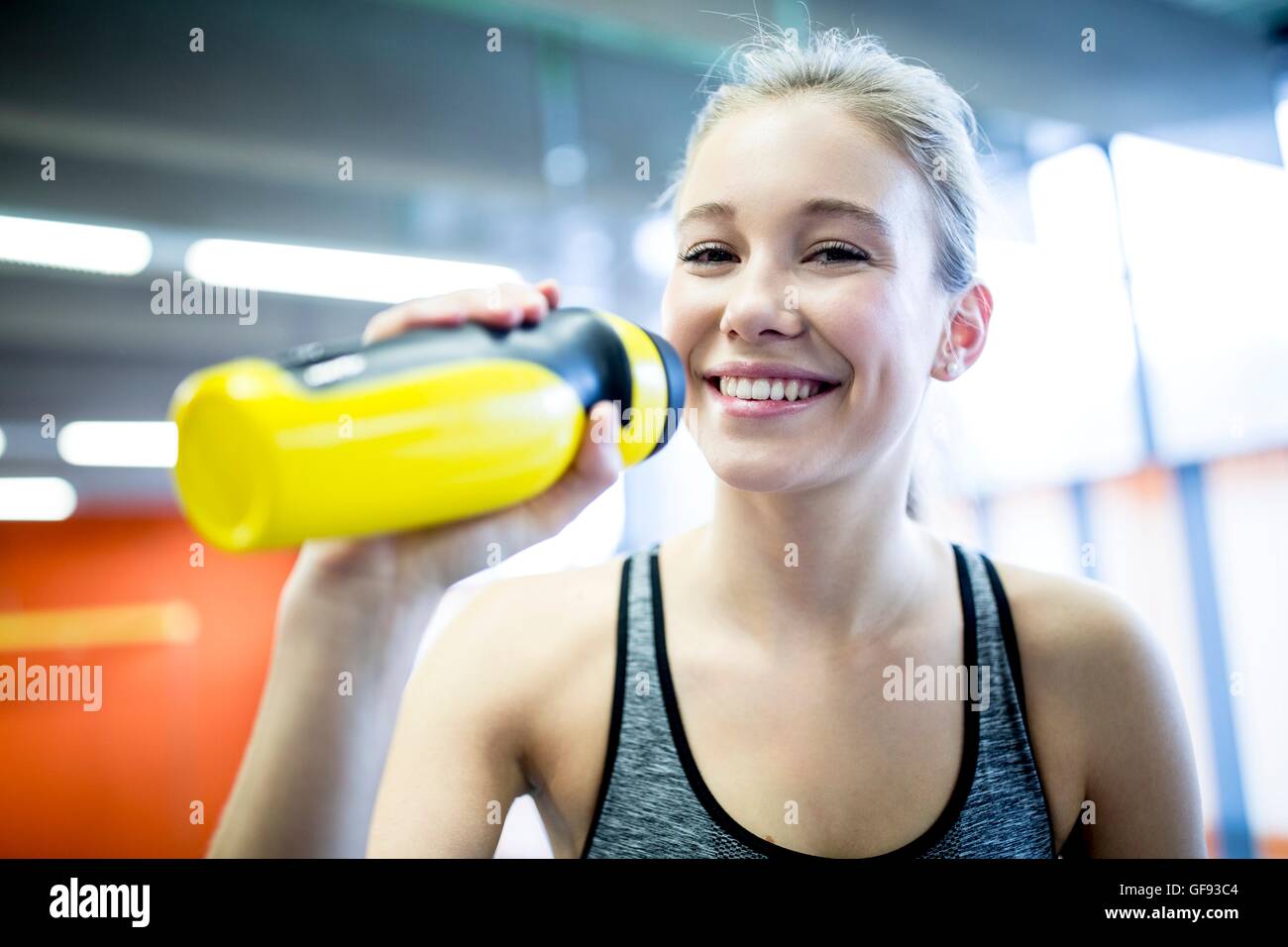 EIGENTUM FREIGEGEBEN. -MODELL VERÖFFENTLICHT. Junge Frau Trinkwasser in Fitness, Lächeln, Porträt. Stockfoto