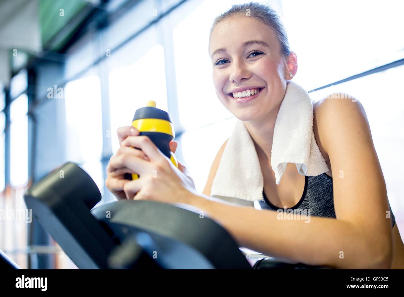 EIGENTUM FREIGEGEBEN. -MODELL VERÖFFENTLICHT. Junge Frau mit Flasche Wasser beim Training im Fitness-Studio, Lächeln, Porträt. Stockfoto