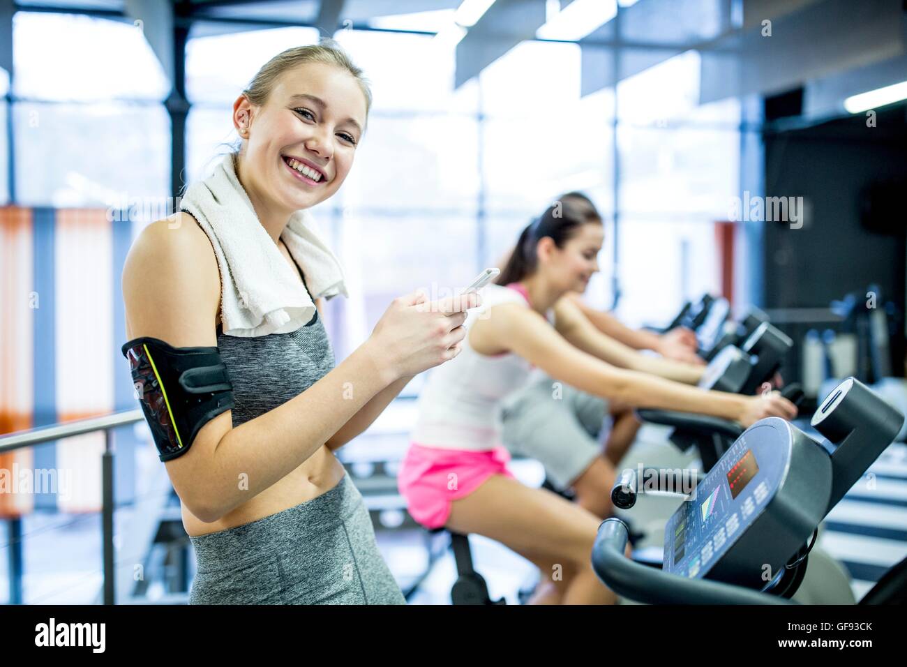 EIGENTUM FREIGEGEBEN. -MODELL VERÖFFENTLICHT. Porträt der jungen Frau SMS auf Handy während der Arbeit im Fitness-Studio, lächelnd. Stockfoto