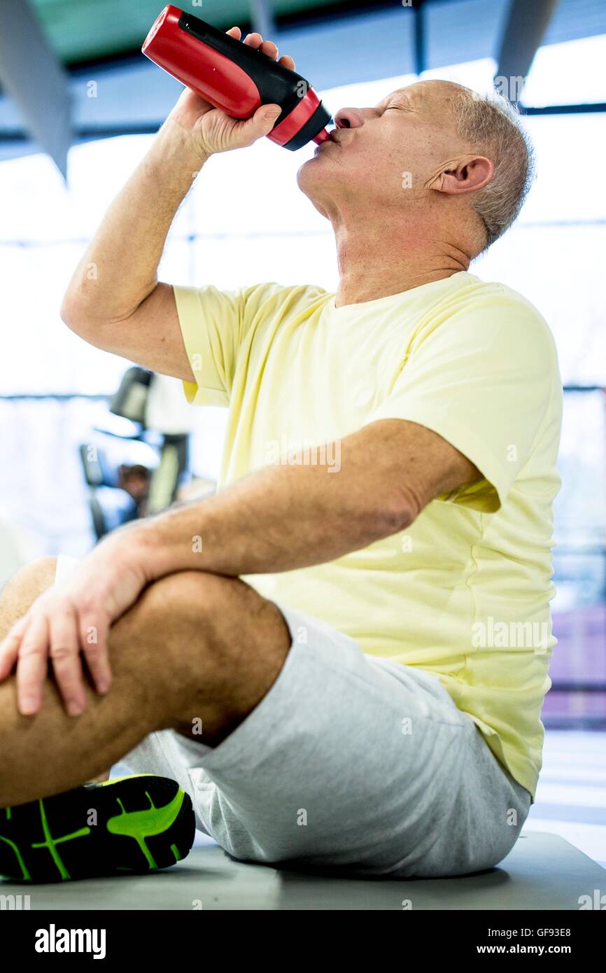 EIGENTUM FREIGEGEBEN. -MODELL VERÖFFENTLICHT. Ältere Mann sitzt und Trinkwasser aus Wasserflasche im Fitness-Studio. Stockfoto