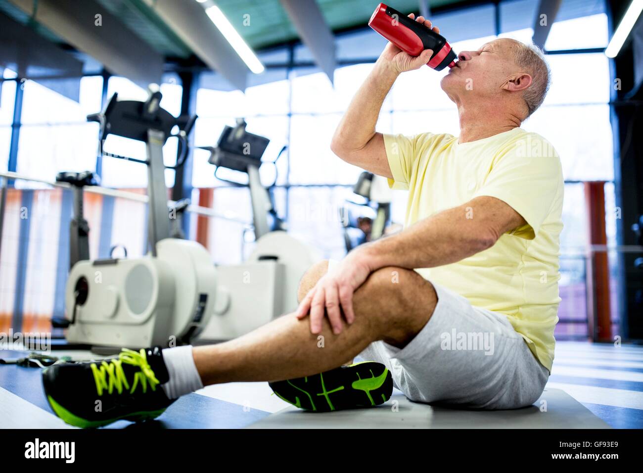 EIGENTUM FREIGEGEBEN. -MODELL VERÖFFENTLICHT. Ältere Mann sitzt und Trinkwasser aus Wasserflasche im Fitness-Studio. Stockfoto