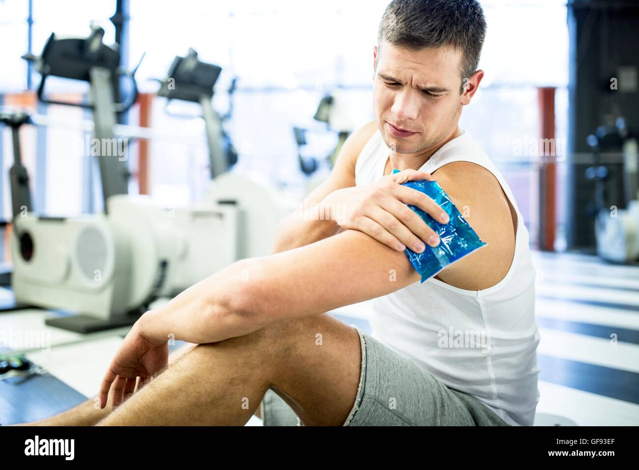 EIGENTUM FREIGEGEBEN. -MODELL VERÖFFENTLICHT. Junger Mann mit Eisbeutel auf verletzte Schulter im Fitnessstudio. Stockfoto