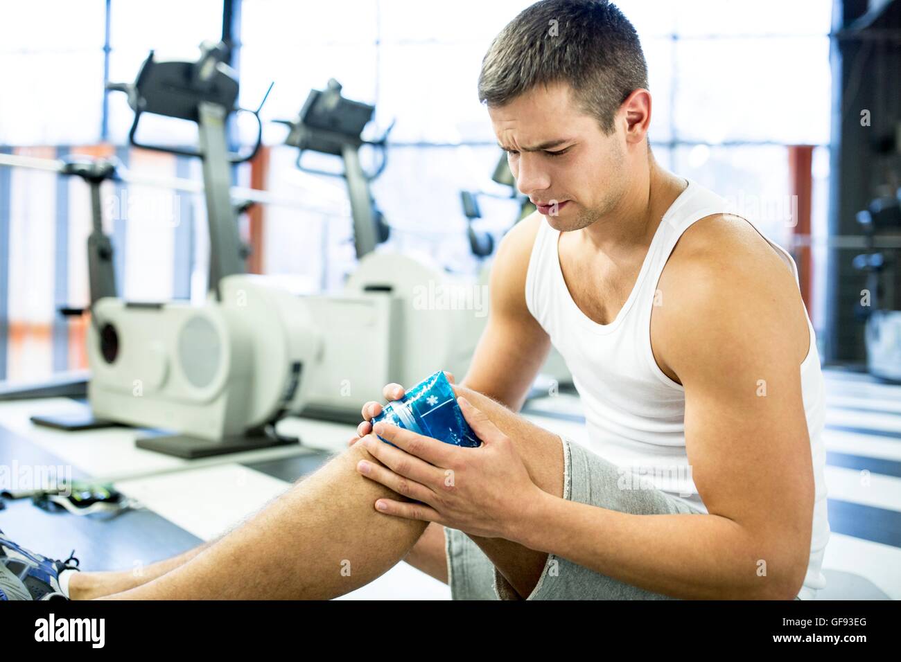 EIGENTUM FREIGEGEBEN. -MODELL VERÖFFENTLICHT. Junger Mann Betrieb Eisbeutel auf verletzte Knie im Fitness-Studio. Stockfoto