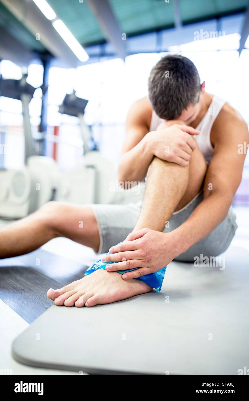 EIGENTUM FREIGEGEBEN. -MODELL VERÖFFENTLICHT. Junger Mann Betrieb Eisbeutel auf verletzten Knöchel im Fitness-Studio. Stockfoto