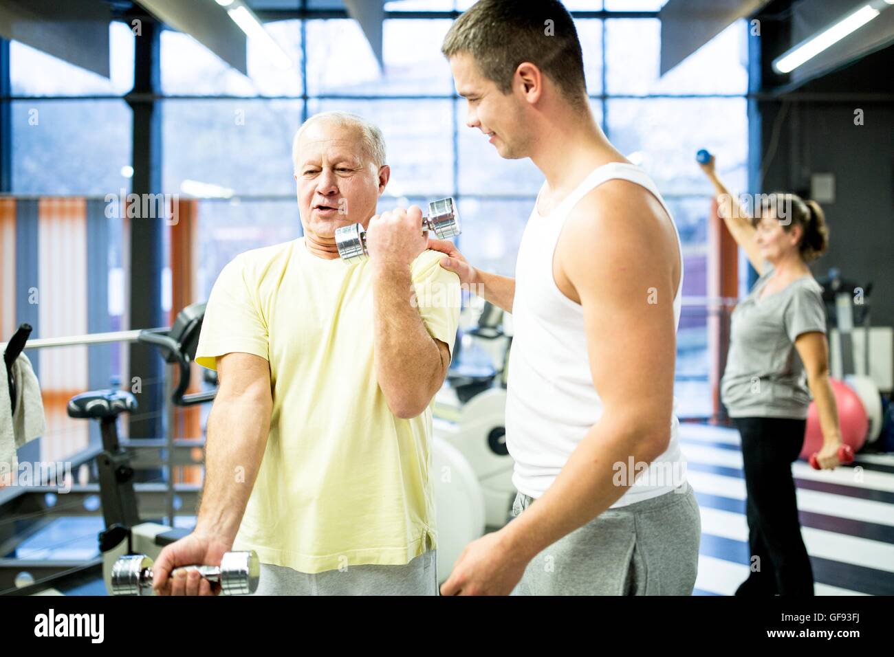 EIGENTUM FREIGEGEBEN. -MODELL VERÖFFENTLICHT. Senior woman Abholung Hanteln mit Trainer im Fitness-Studio helfen. Stockfoto