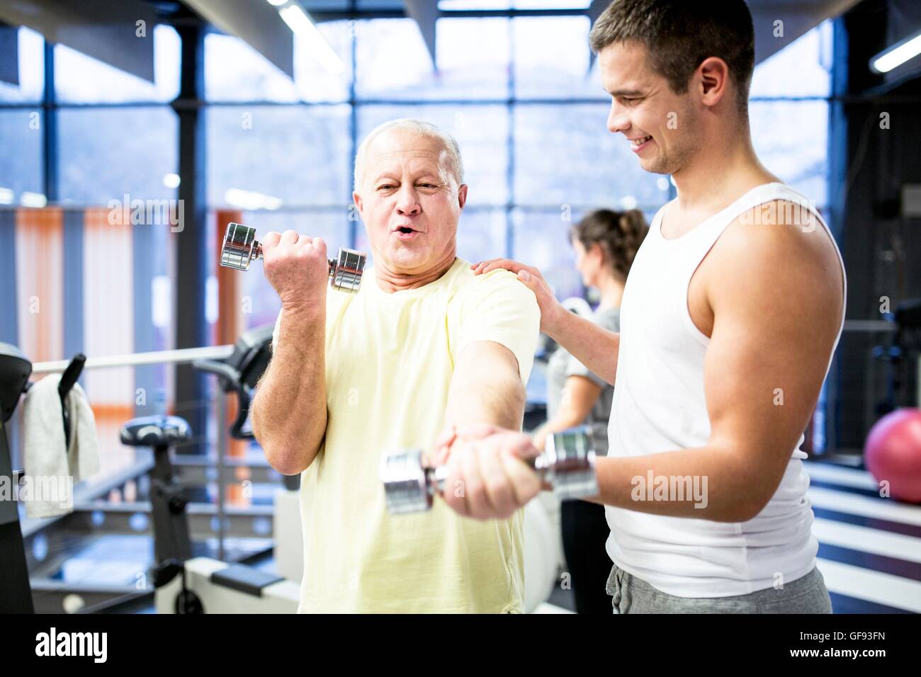 EIGENTUM FREIGEGEBEN. -MODELL VERÖFFENTLICHT. Senior woman Abholung Hanteln mit Unterstützung der Trainer im Fitness-Studio. Stockfoto