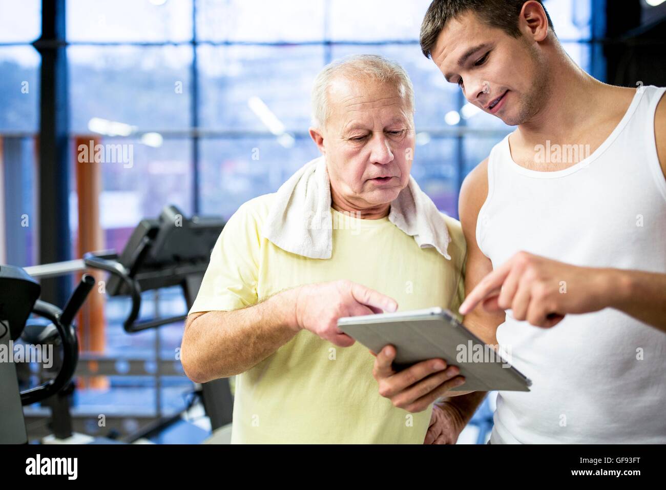 EIGENTUM FREIGEGEBEN. -MODELL VERÖFFENTLICHT. Junge Gym Trainer zeigt Tablet senior Mann nach dem Training im Fitness-Studio. Stockfoto