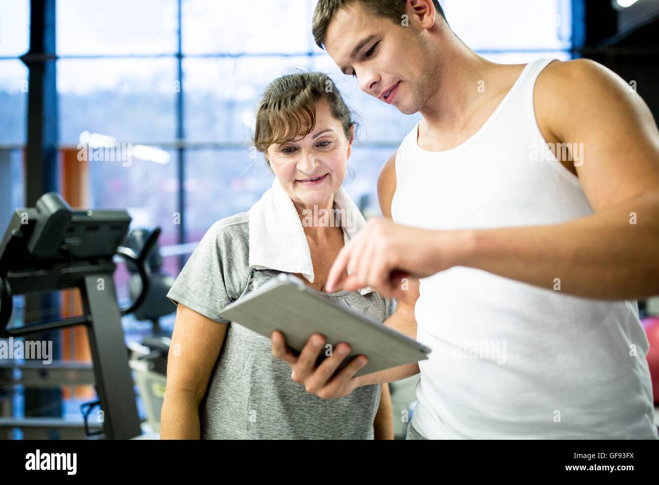 EIGENTUM FREIGEGEBEN. -MODELL VERÖFFENTLICHT. Junge Gym Trainer zeigt Tablet senior Frau im Fitness-Studio. Stockfoto