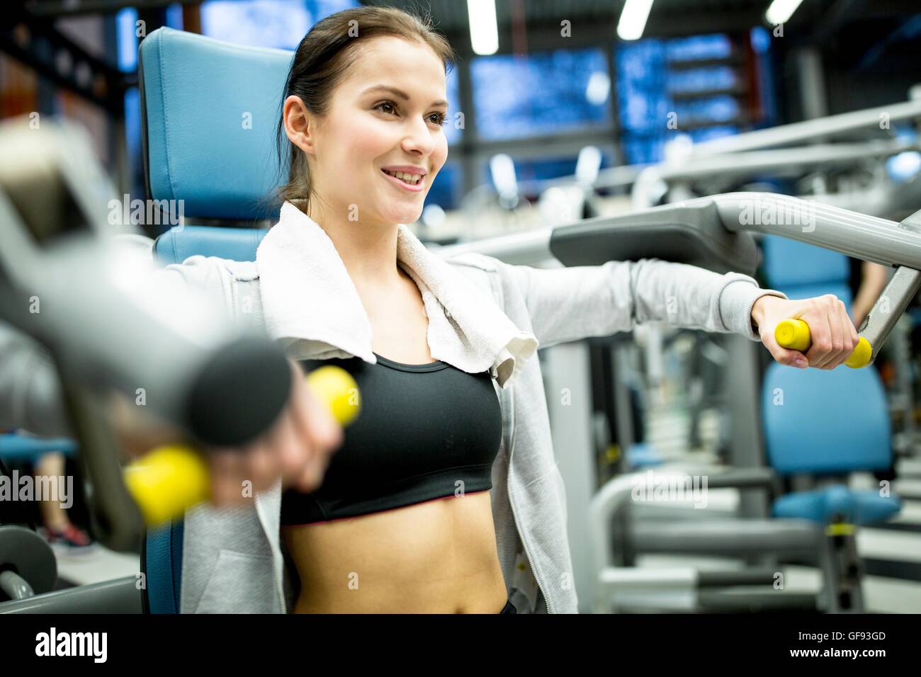 EIGENTUM FREIGEGEBEN. -MODELL VERÖFFENTLICHT. Junge Frau lächelnd und mit Ausübung Maschine in Fitness-Studio. Stockfoto