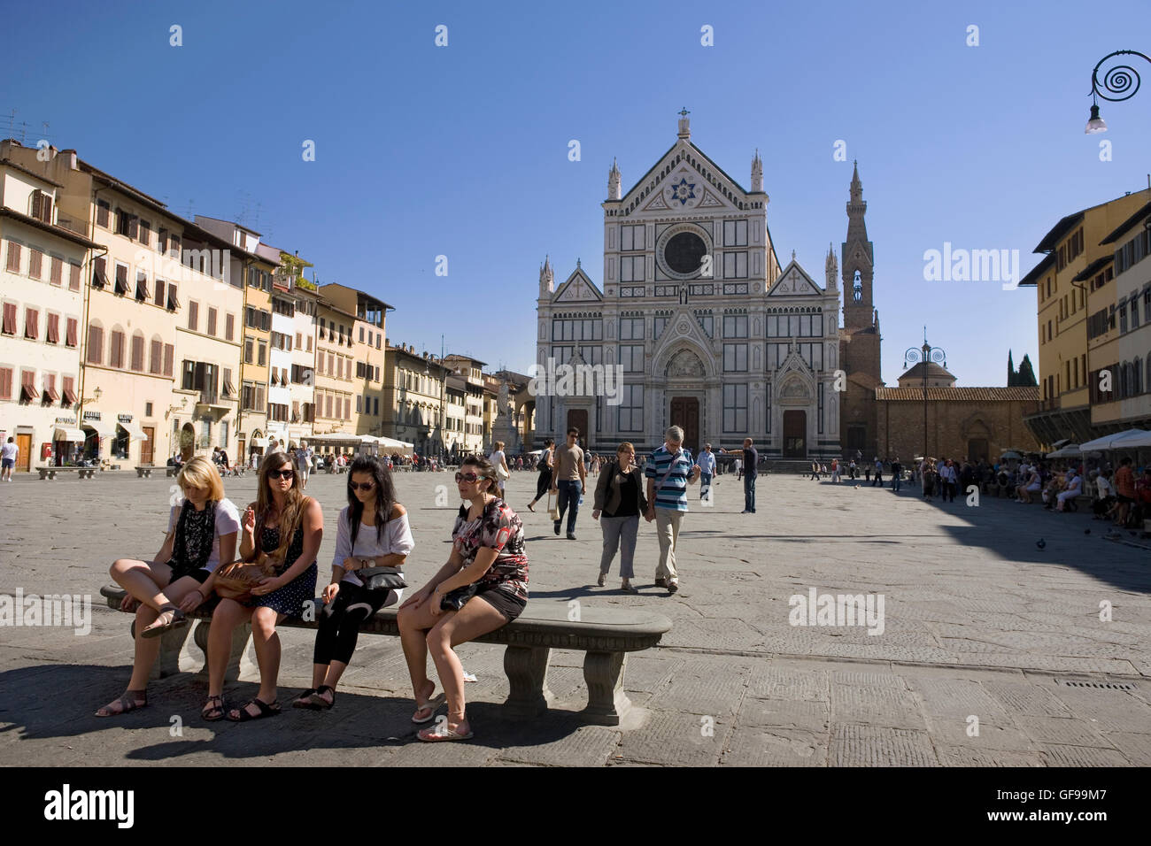 Vier Mädchen sitzen auf einer Bank auf der Piazza di Santa Croce, Florenz, Toskana, Italien, mit der Basilika des Heiligen Kreuzes hinter Stockfoto
