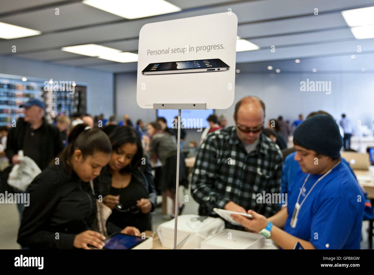 Ein Apple Mitarbeiter (R, blaues Hemd) zeigt einem Client (2R) seine neue iPad neben einem Schild einrichten, die liest "persönliches Setup in Pr Stockfoto