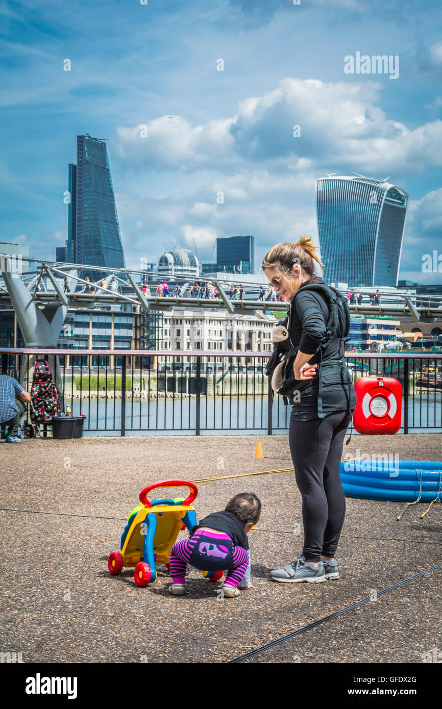 Eine Mutter und ein Baby mit einem kleinen Wanderer am Ufer der Themse in der Nähe der Tate Modern, London, England, Großbritannien Stockfoto