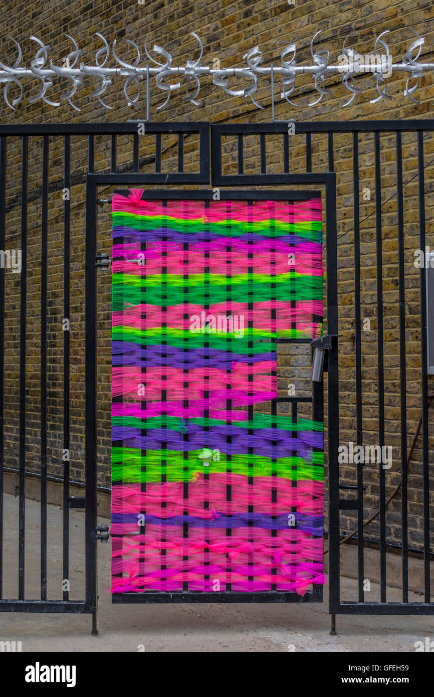 Hässliche schwarze Stahl Sicherheits-Tor verwandelt mit leuchtenden Multi farbige Gewinde in knalligem Pink, grün und lila, Landor unterwegs, Stockfoto