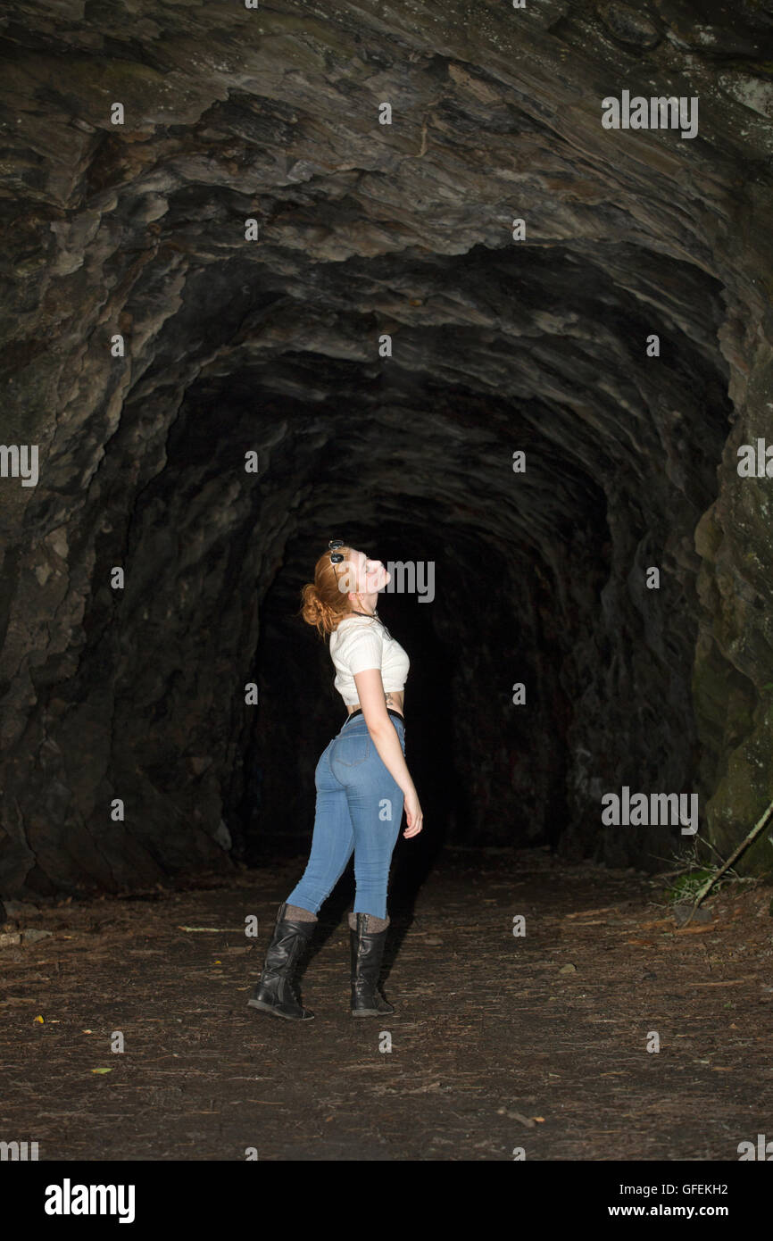 Schöne rote Kopf in Röhrenjeans, schwarzen Stiefeln und weißen Oberteil, stehend an der Mündung des einen tiefen Tunnel in einer Granitklippe. Stockfoto