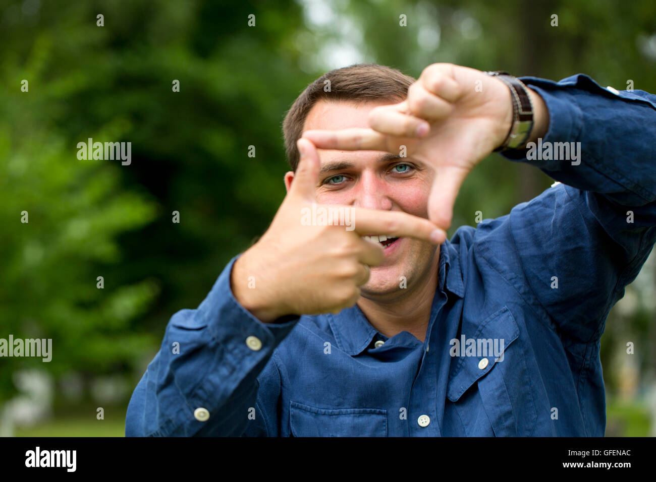 Ein Mann auf der Suche und Fokussierung durch seine Hände auf grünen Sommer Hintergrund Stockfoto