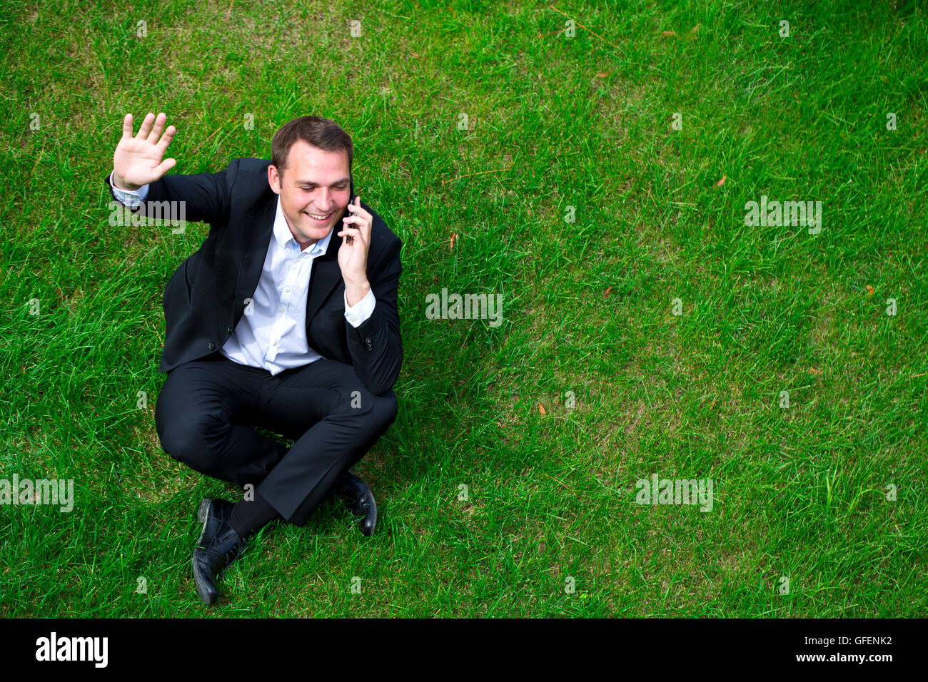 Fröhliche junge Geschäftsmann Aufruf per Telefon sitzen auf dem grünen Rasen Stockfoto