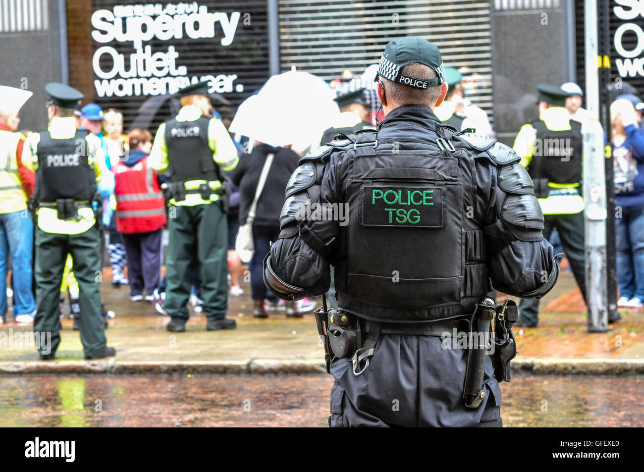 Belfast, Nordirland. 10. August 2014 - Polizeibeamte halten eine Menschenmenge unter Kontrolle, während ein Mitglied der taktischen Unterstützungsgruppe (Aufruhr) den Fortschritt beobachtet Stockfoto