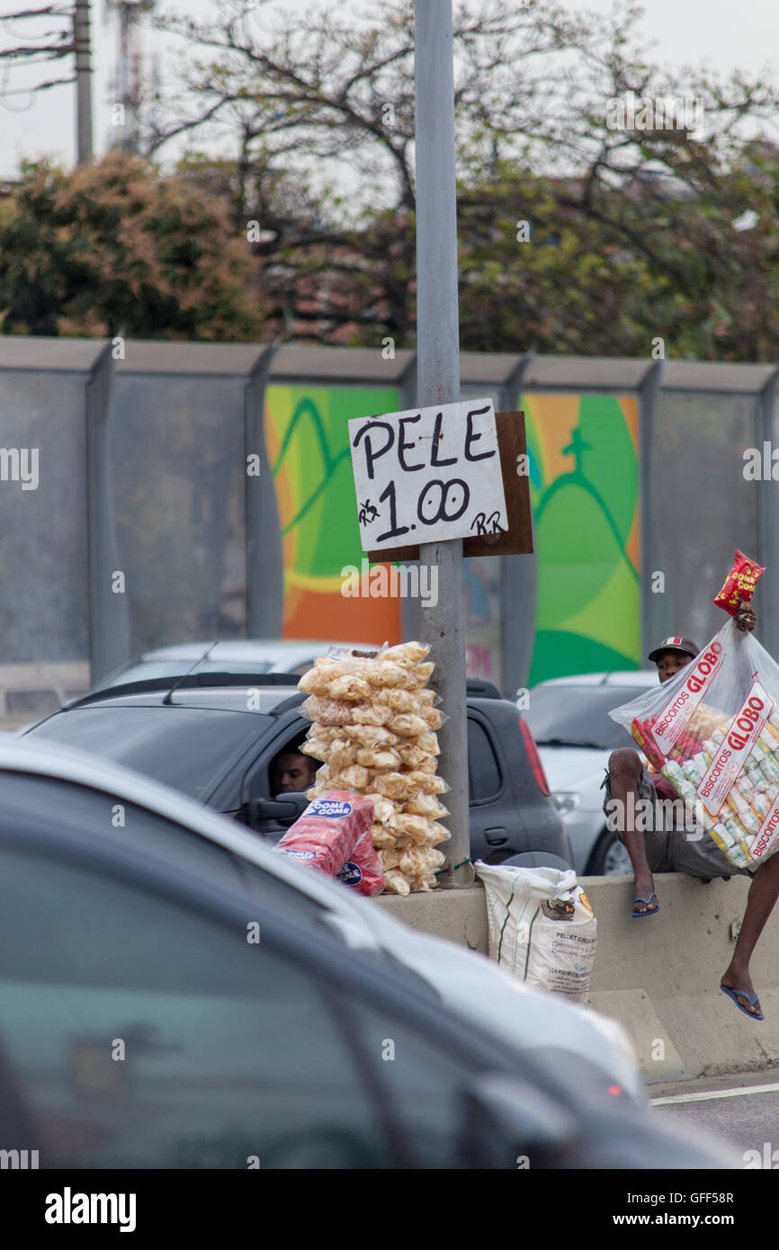 Bewohner von Complexo da Mare, einer massiven Netzwerk der Favelas, die neben der Linha Vermelha (rote Linie), die Autobahn vom Flughafen in die Innenstadt, Rio De Janeiro sitzt arbeiten als Straßenverkäufer während der Stoßzeiten an der Expreessway - seit 2010 ist die Gemeinschaft eingezäunten Weg von der Autobahn durch riesige Plexiglas Platten - Behörden behaupten sie bieten eine akustische Barriere , einheimischen beschreiben es als eine "Mauer der Schande", anders Arme Menschen zu verstecken. Stockfoto