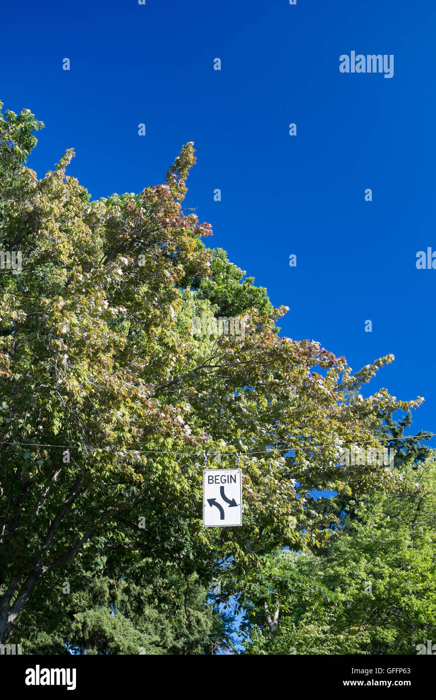 Begin zwei weg drehen Schild mit Bäumen und blauen Himmel Stockfoto