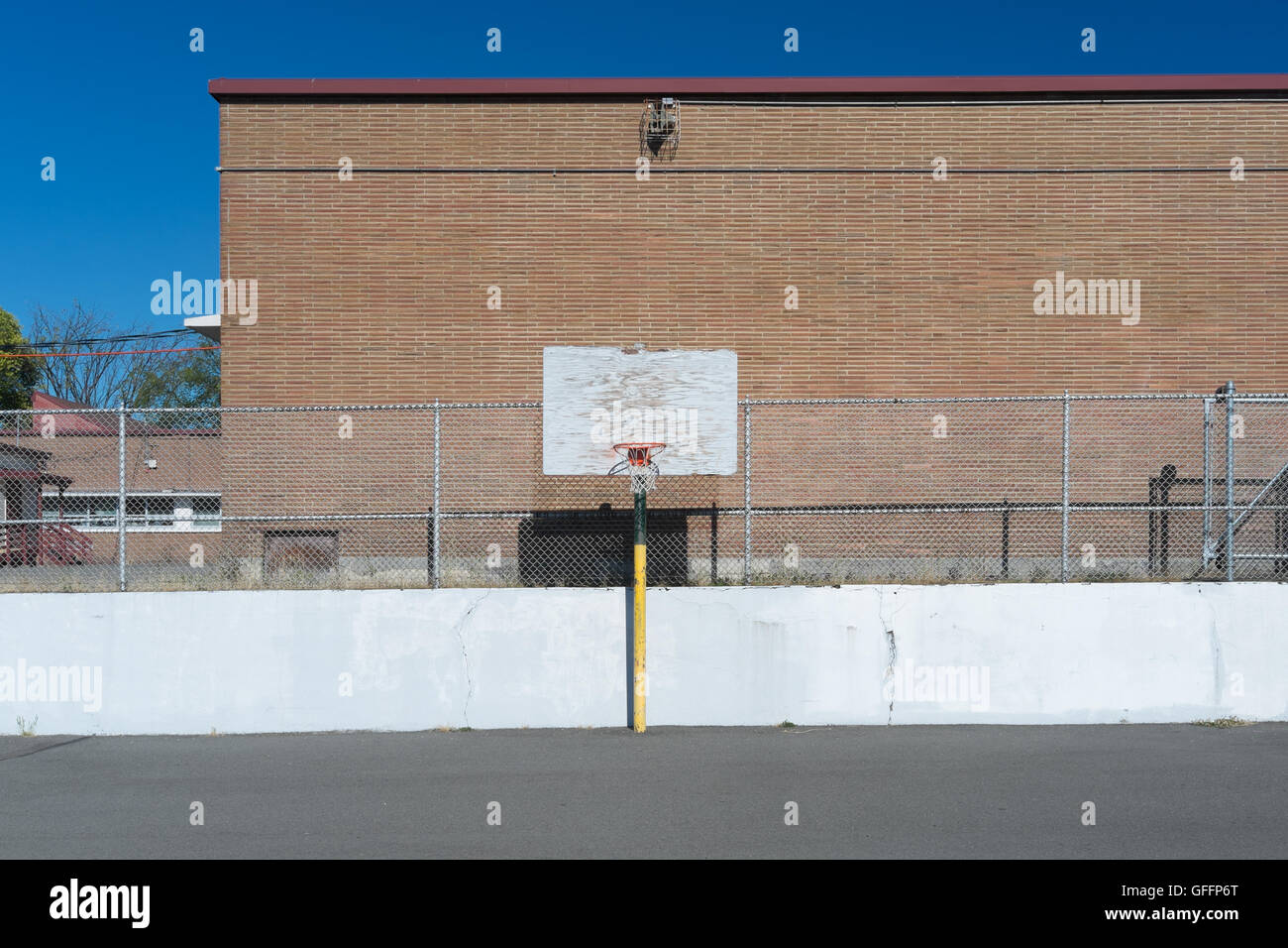 institutionelle Basketballkorb mit einem Holz oder Holz Rückwand mit einer Ziegelwand, Maschendrahtzaun und einer Betonwand und ein blauer Himmel im Hintergrund Stockfoto