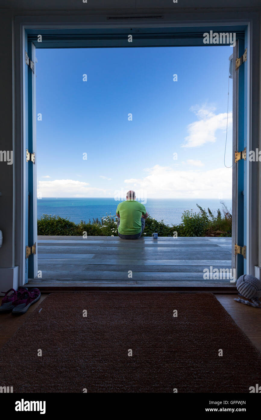Eine Person sitzt auf der Terrasse eines Ferienhauses bei Tregonhawke Cliff, Whitsand Bay, Cornwall, England, UK Stockfoto