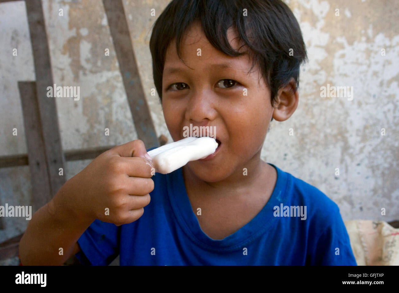 Ein kleiner Junge isst eine Eis-Bar in einem Slum in Kampong Cham, Kambodscha. Stockfoto