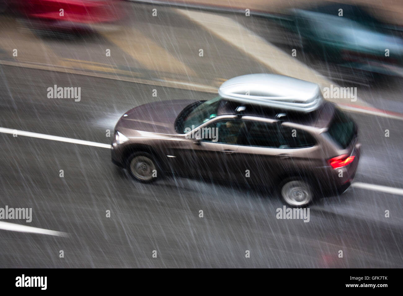 Regnerischen Tag in der Stadt: ein fahrendes Auto mit einer Aufbewahrungsbox auf dem Dach, auf der Straße getroffen durch Starkregen mit Hagel, in Bewegung b Stockfoto