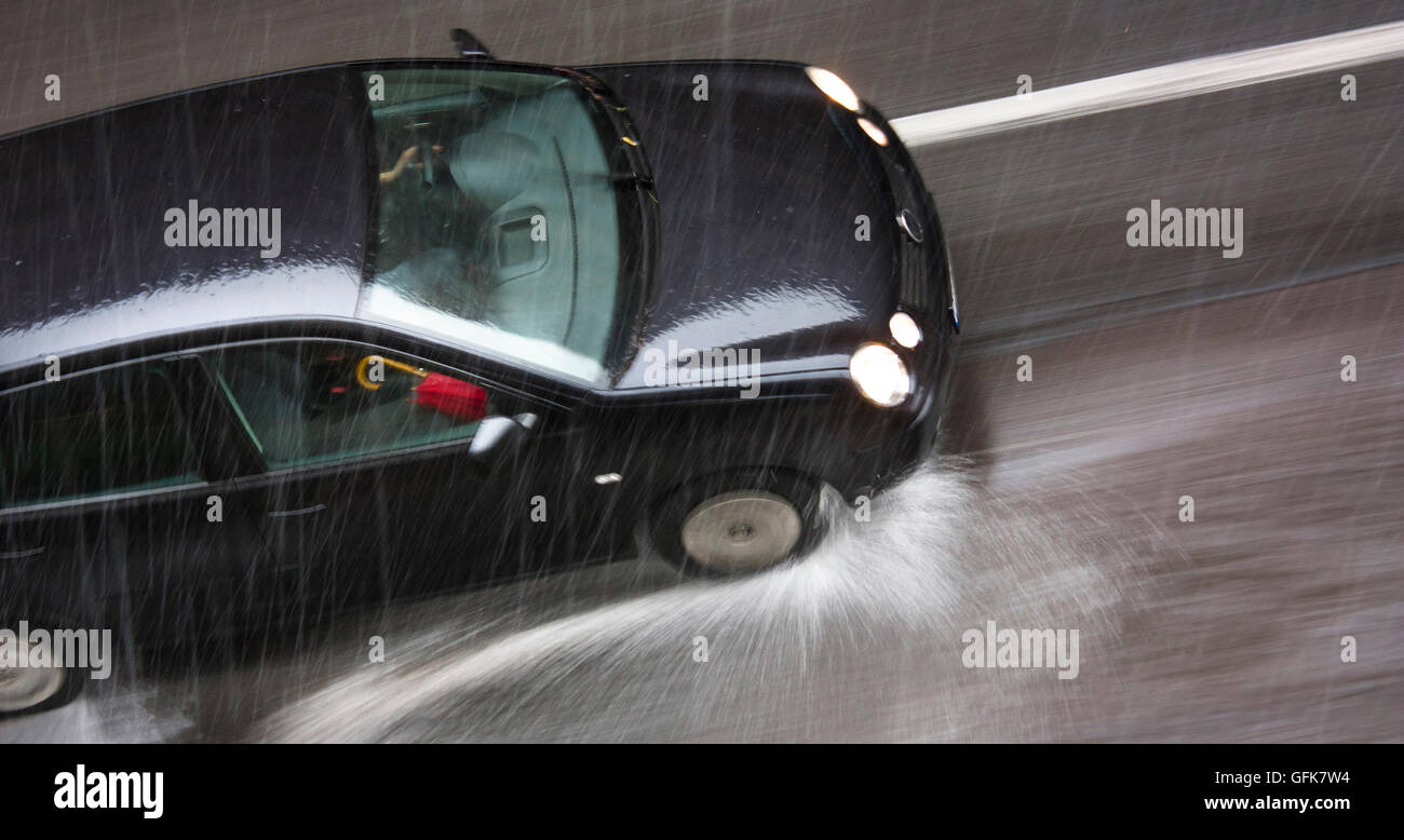Regnerischen Tag in der Stadt: ein fahrendes Auto, mit einem roten Regenschirm auf dem Vordersitz in der Stadtstraße, getroffen durch Starkregen mit Hagel Stockfoto