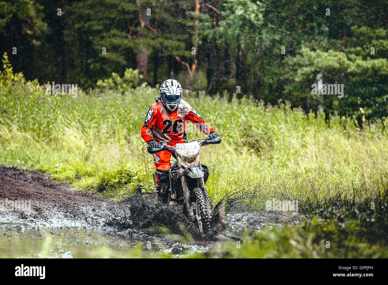 Motorrad Racer Fahrten in einer Pfütze Schlamm im Wald um ihn herum Wasserspritzer beim Ural Cup in enduro Stockfoto