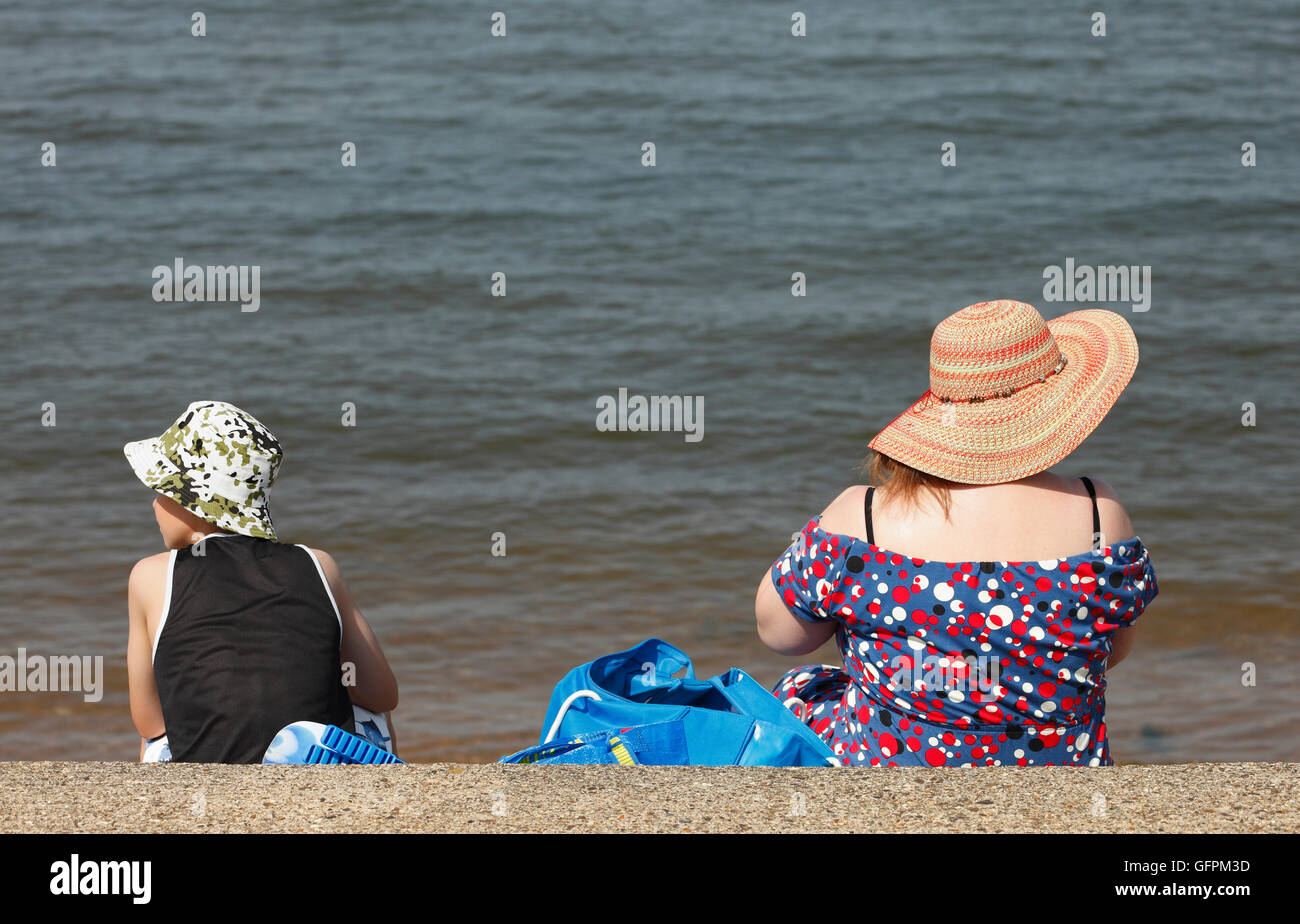 Mutter und Sonne an der Küste tragen Hüte an einem heißen Sommertag. Stockfoto