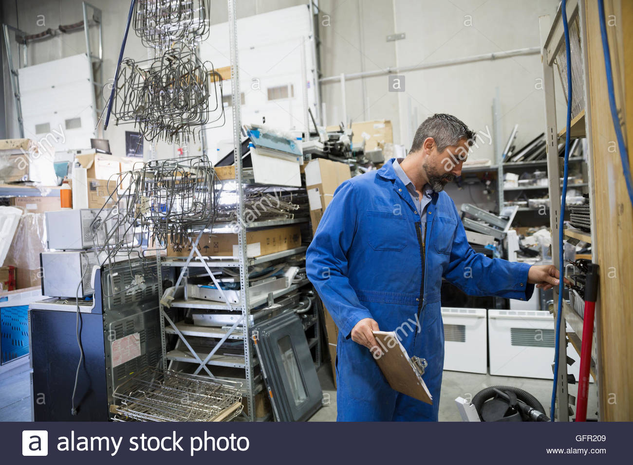 Arbeiter in Overalls mit Zwischenablage im Gerät-Reparatur-Werkstatt Stockfoto