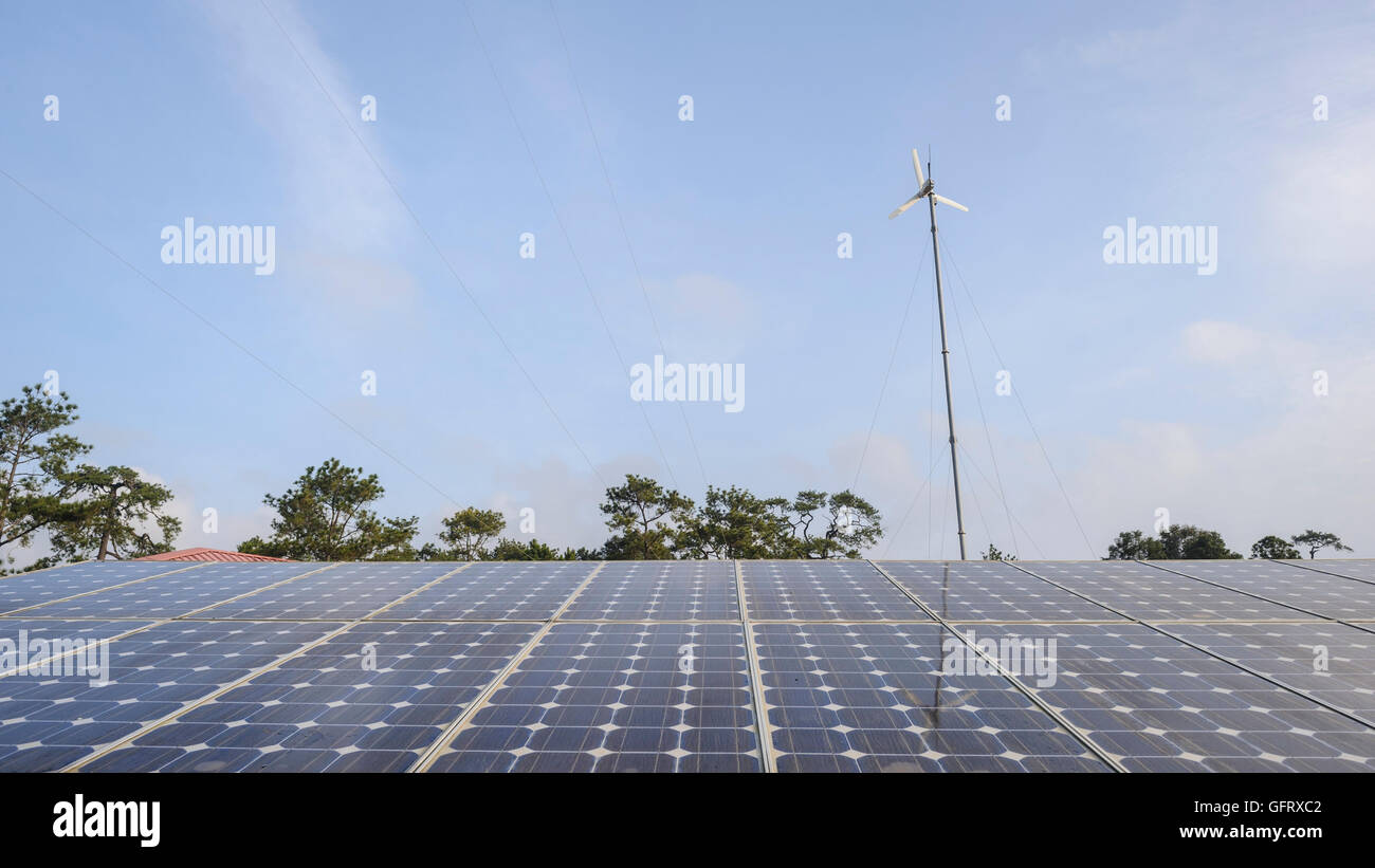 Raster-Sonnenkollektoren und Windkraftanlage mit blauem Himmel in Landschaft. Stockfoto