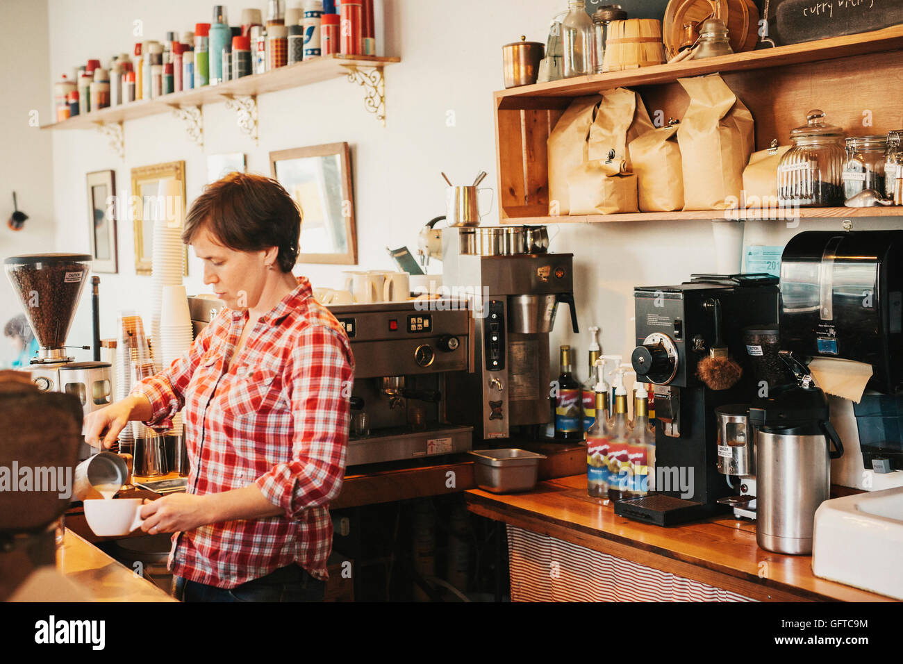 Eine Frau in einem karierten Hemd hinter dem Tresen in einem Café arbeiten Stockfoto