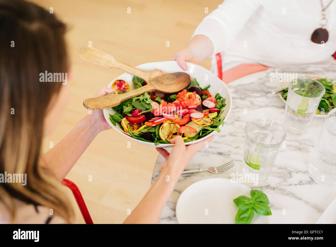 Ansicht von oben eine Tabelle mit Besteck und Teller von zubereiteten Speisen eine Frau hält einen Salatteller gelegt Stockfoto