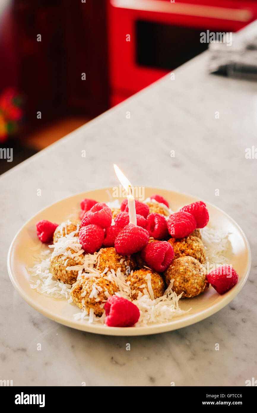 Eine Platte mit einem Dessert und frische Himbeeren und einer beleuchteten Geburtstag Kerze Stockfoto