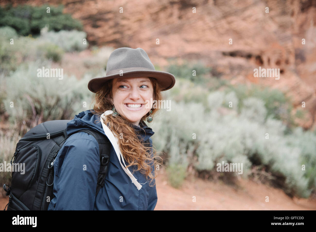 Lächelnde Frau mit kastanienbraunen Haaren trägt einen Hut und Rucksack in einem Canyon Wandern Stockfoto