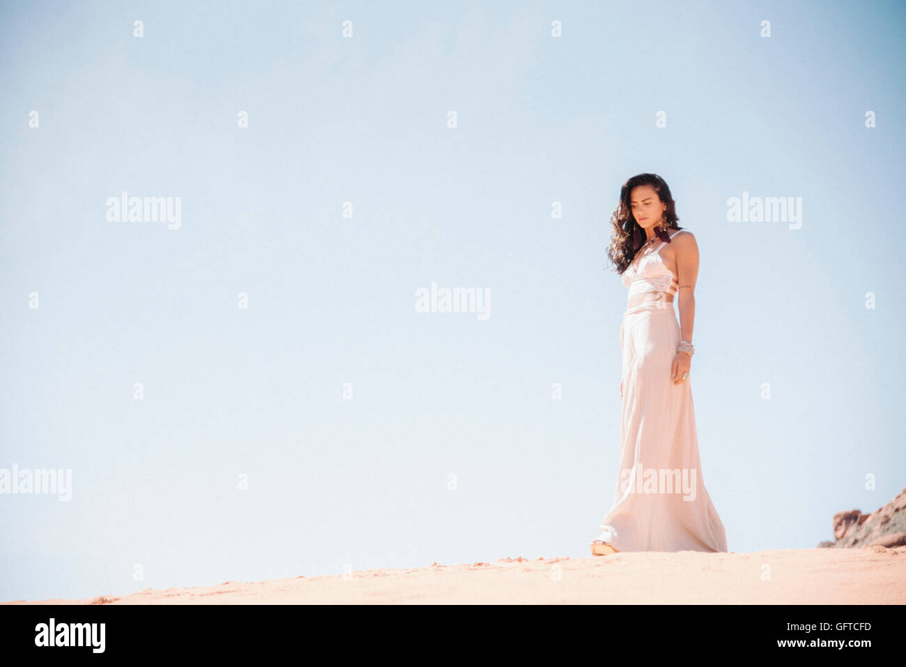 Junge Frau mit langen braunen Haaren, trägt ein langes weißes Kleid steht in der Wüste Stockfoto
