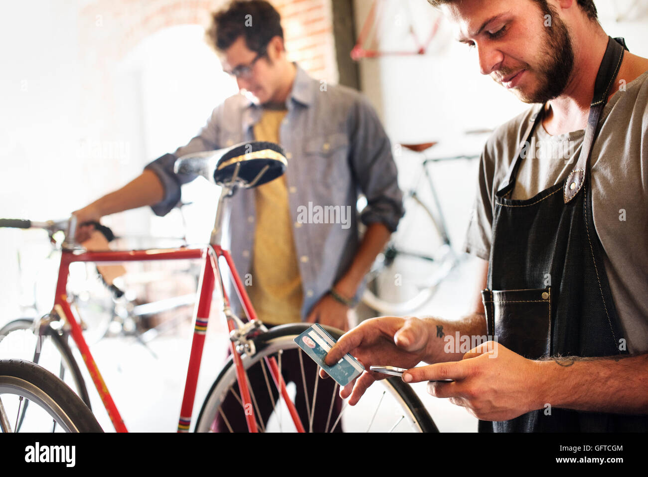 Zwei Männer in einem Zyklus-Werkstatt ein Betrieb, ein Smartphone und Kredit Karte bezahlen durch kontaktlose Karte Stockfoto