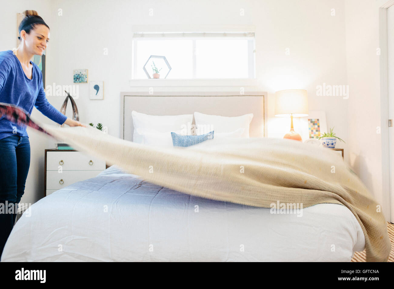 Eine Frau, die eine schlichte Decke auf ein Doppelbett in einem hellen luftigen Wohnung Schlafzimmer verteilen Stockfoto