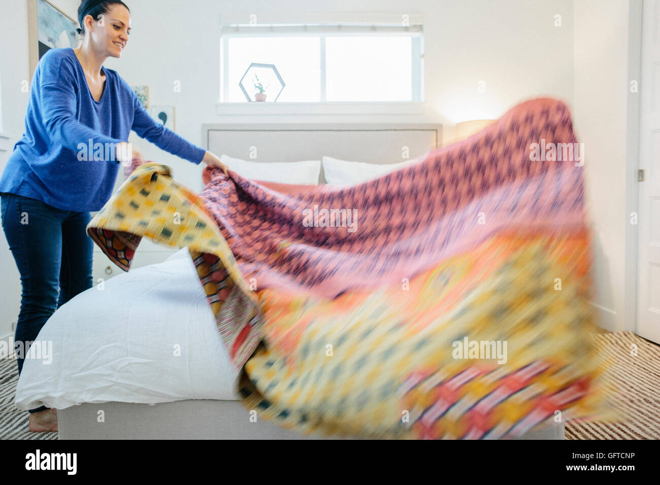 Eine Frau, die Verbreitung eines bunten gemusterten Quilts über ein Doppelbett Stockfoto