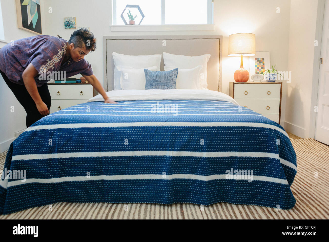 Eine Frau, die Glättung einer blaues gestreift werfen über ein Doppelbett im Schlafzimmer Stockfoto