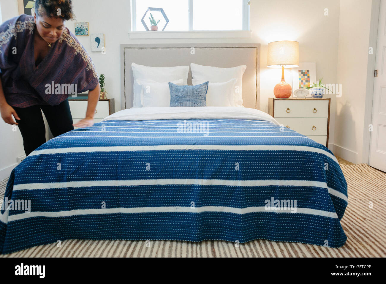 Eine Frau, die Glättung einer blaues gestreift werfen über ein Doppelbett im Schlafzimmer Stockfoto