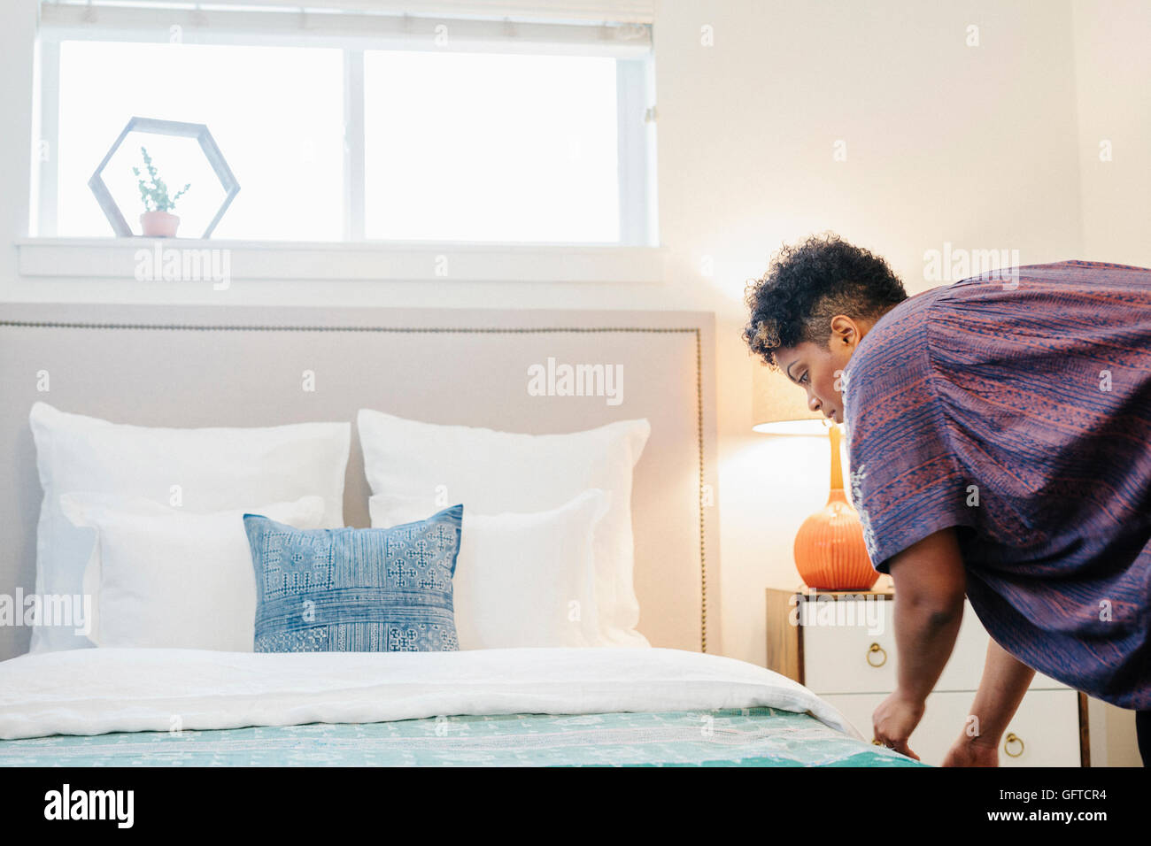 Eine Frau macht ein Doppelbett mit Bettwäsche und Kissen und einem blauen Wurf Stockfoto
