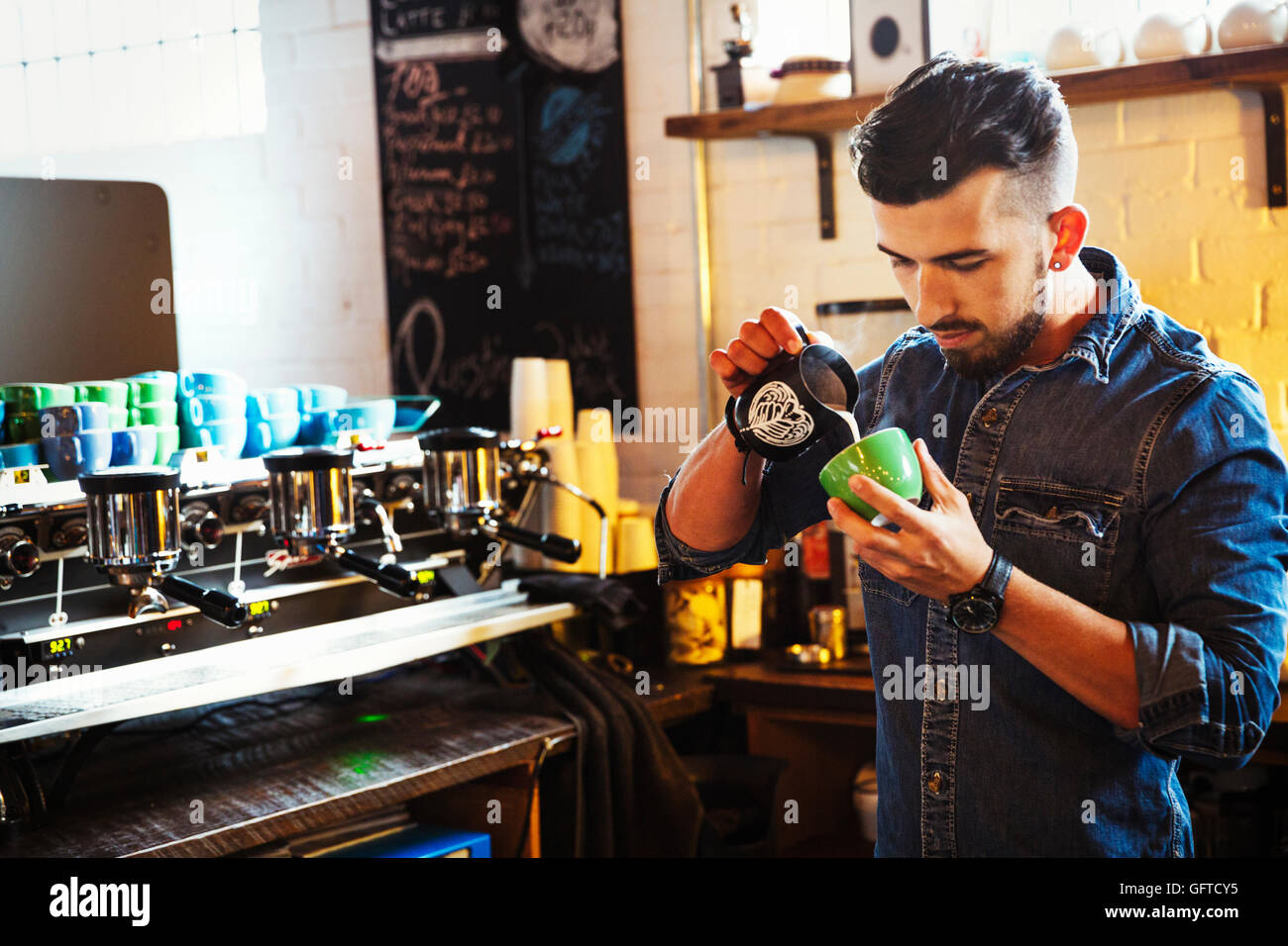 Ein Mann bereitet Cappuccino-Schaum-Muster in eine Kaffeetasse zu schaffen Stockfoto