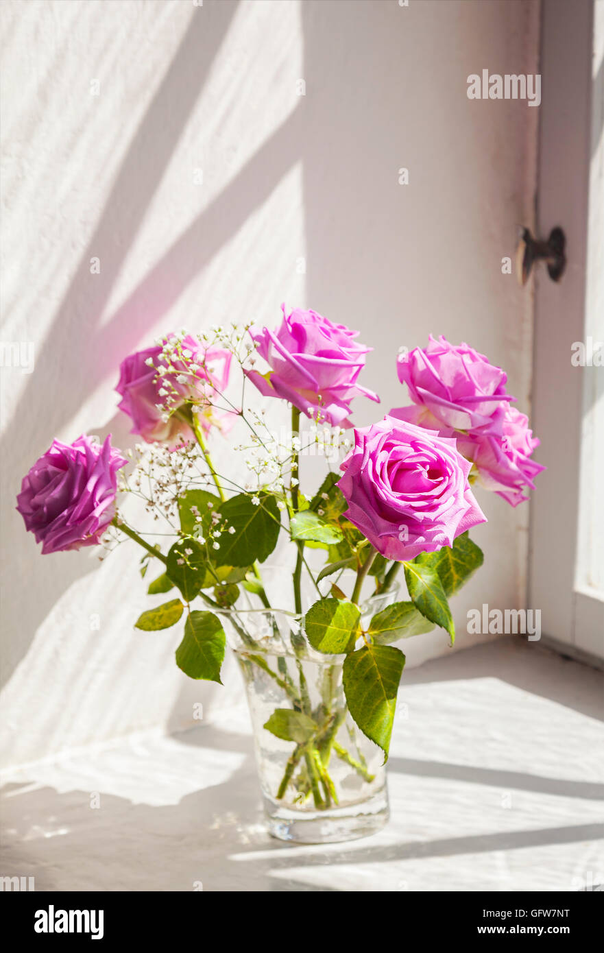 Bild der romantischen Szene mit rosa Rosen in einer Vase von einem alten Fenster. Stockfoto