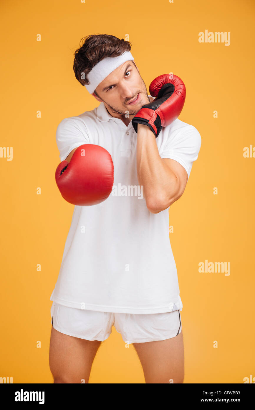 Aggressive junger Mann Boxer in rote Handschuhe Aufwärmen und bereit um zu kämpfen auf gelbem Hintergrund Stockfoto
