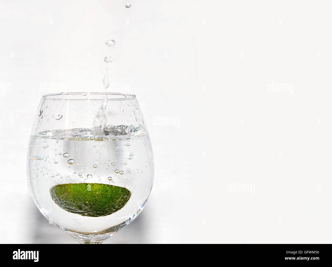 Ein Stück von Kalk Fallenlassen in ein Glas Limonade auf weißem Hintergrund auf der linken Seite Stockfoto