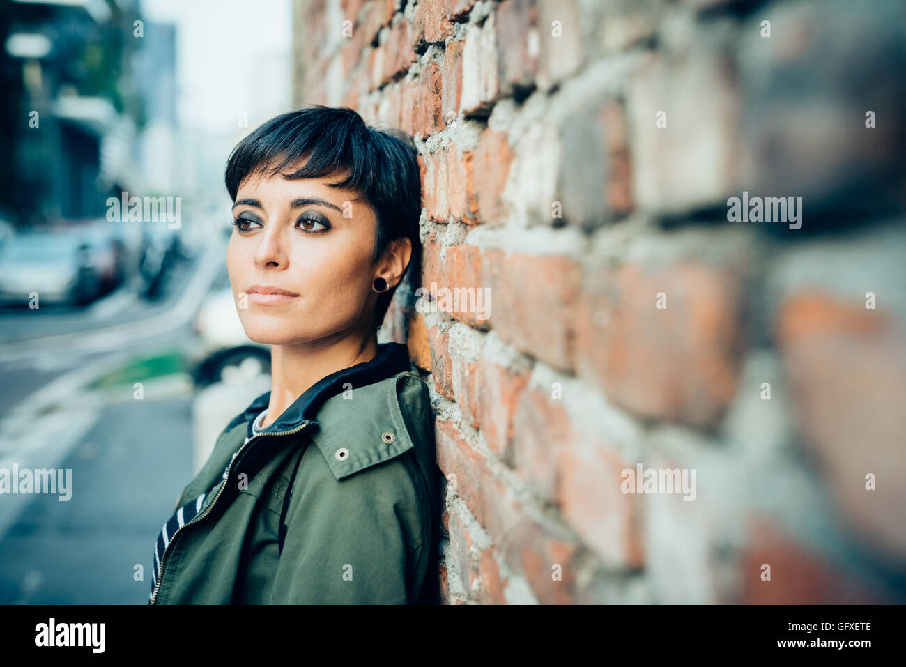 Halbe Länge des jungen schönen kaukasischen braun glattes Haar Frau posiert eine Wand gelehnt, auf der Suche gerade, nachdenklich - ernst, durchdachtes Konzept Stockfoto